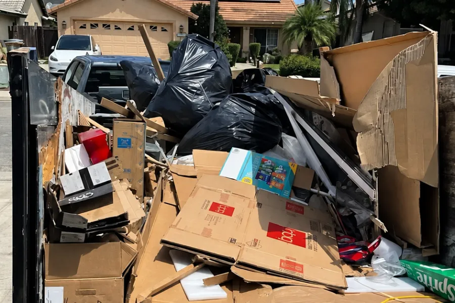 Haulo dump trailer on a residential street loaded with flattened cardboard boxes, packaging foam and bagged household trash