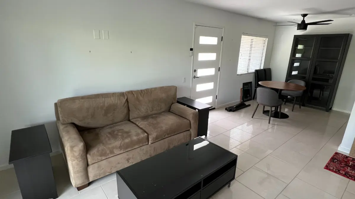 An Anthem living room with a tan sofa, a black media console and a dining set on white tile