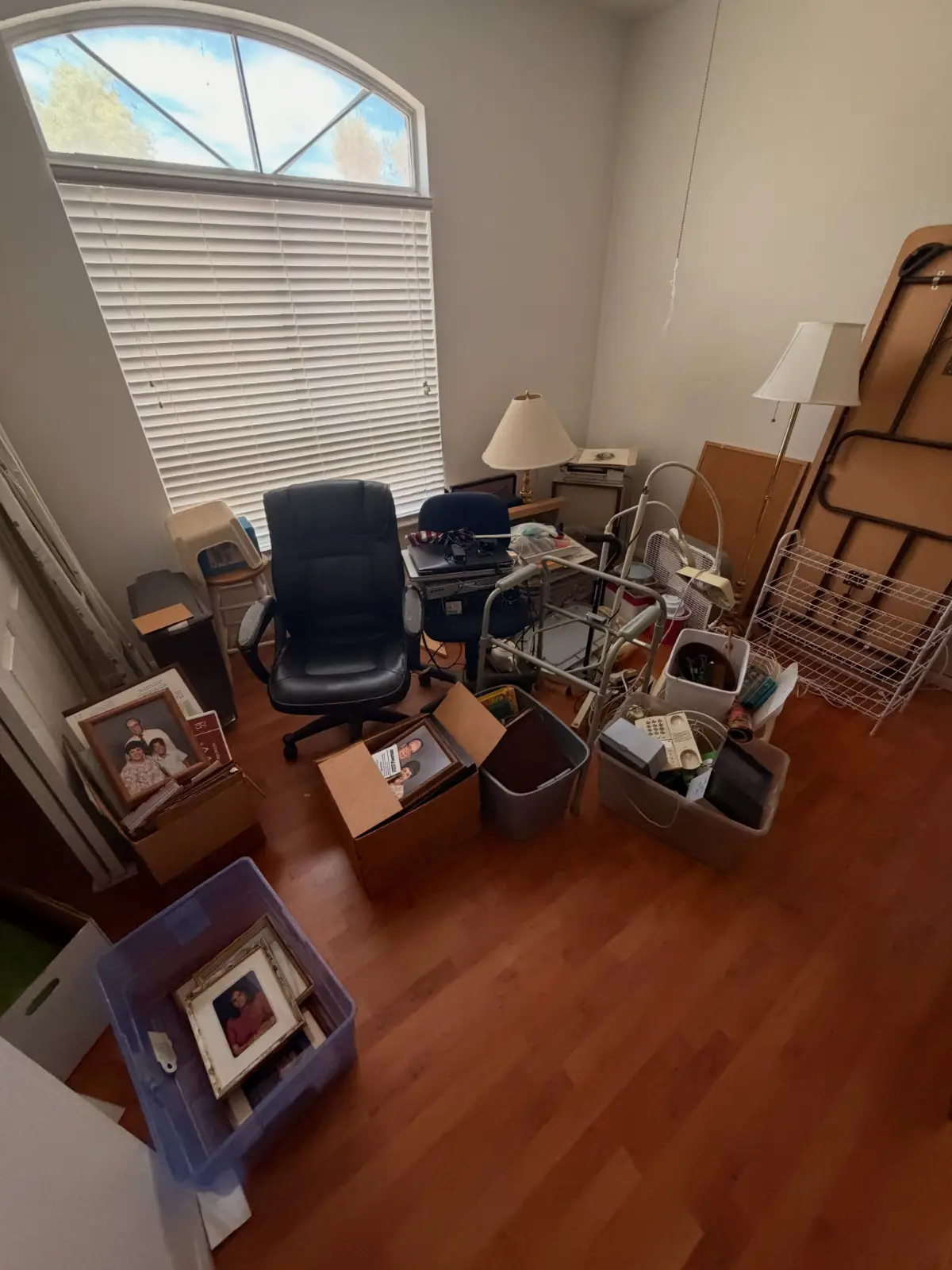 A Carefree home office loaded with an office chair, lamps, framed pictures, bins and boxes under an arched transom window