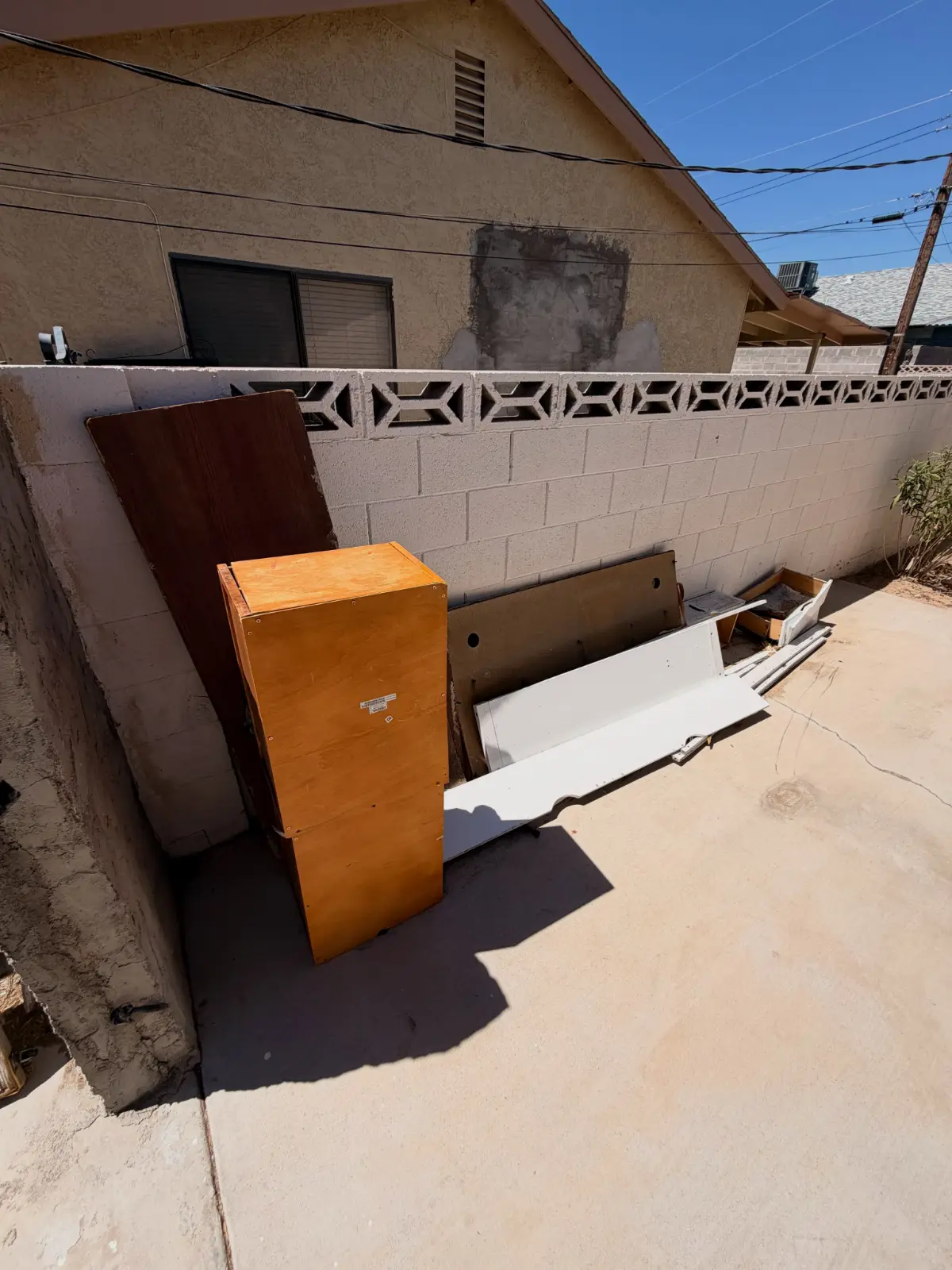 A wooden cabinet, headboard, door and trim leaning against a block wall on a Cave Creek side patio