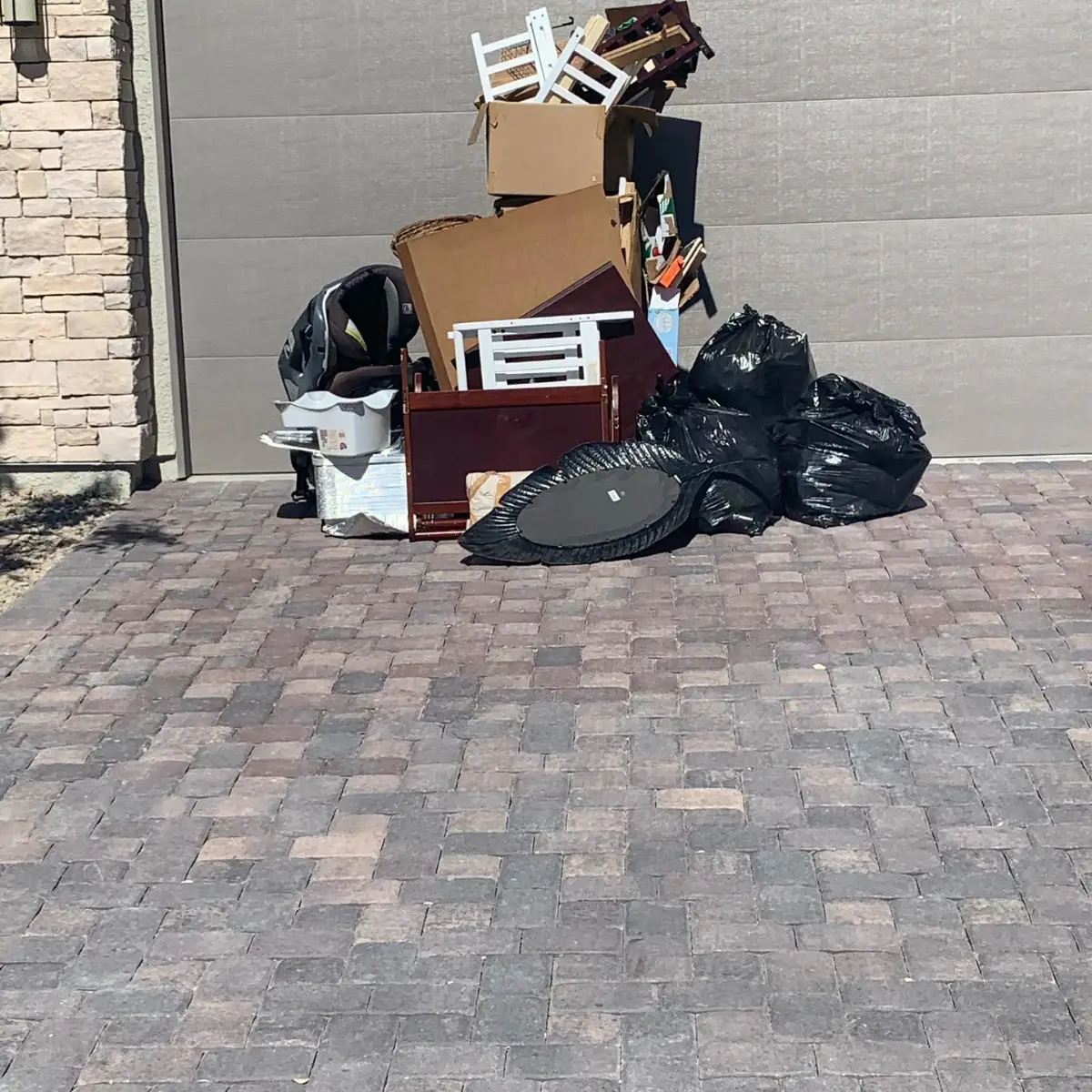 A crib, folding chairs, car seat, bagged items and cardboard stacked on a Cave Creek paver driveway