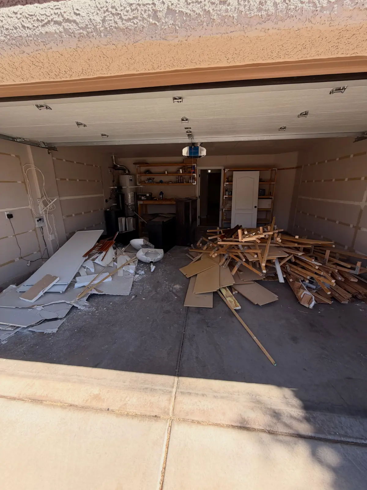 Demolition lumber, drywall and cabinet panels piled across a two-car garage floor in Chandler