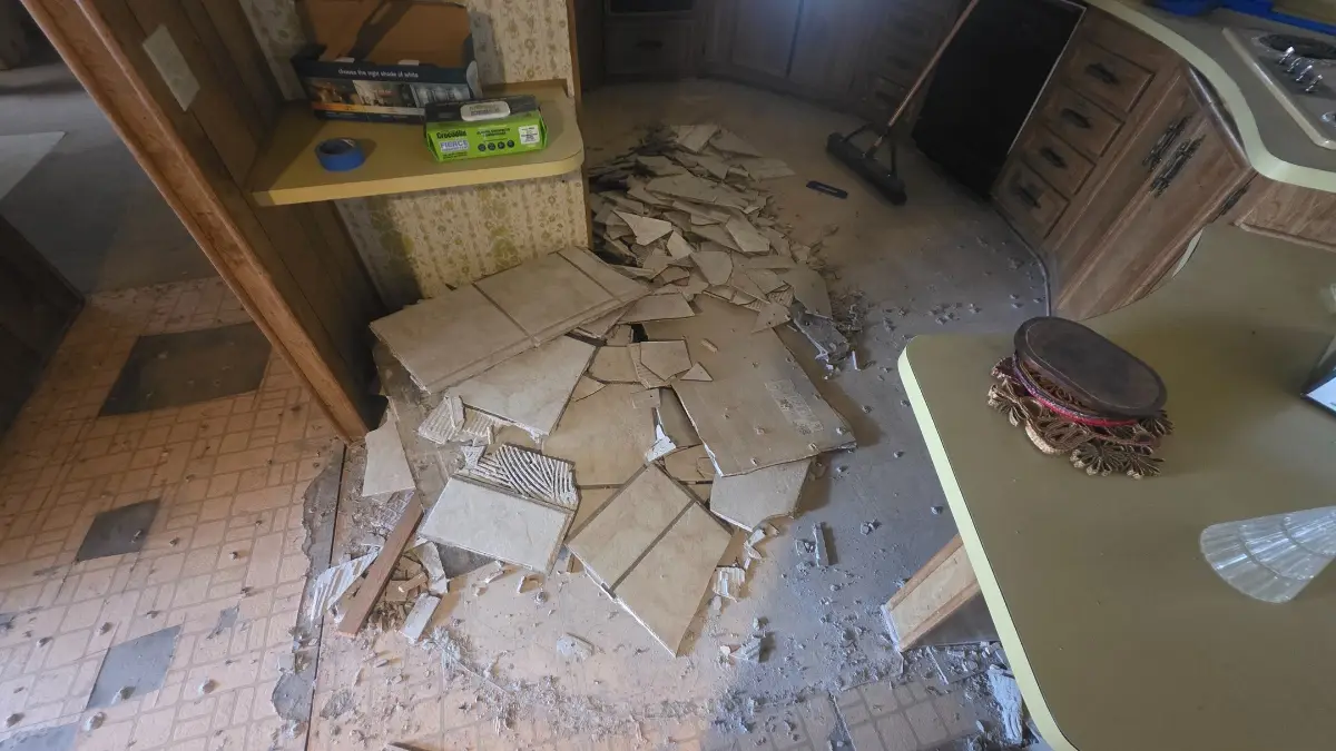 A Chandler mobile-home kitchen floor covered in broken tile and demolition debris between the cabinets