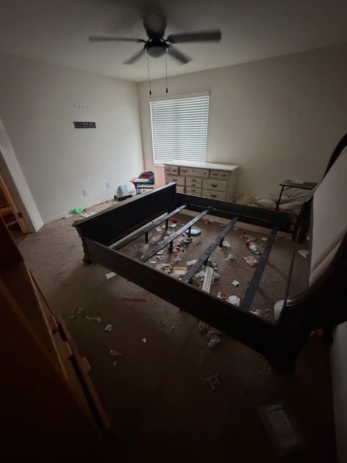 A Chandler bedroom with a bare bed frame, a dresser and refuse on the carpet