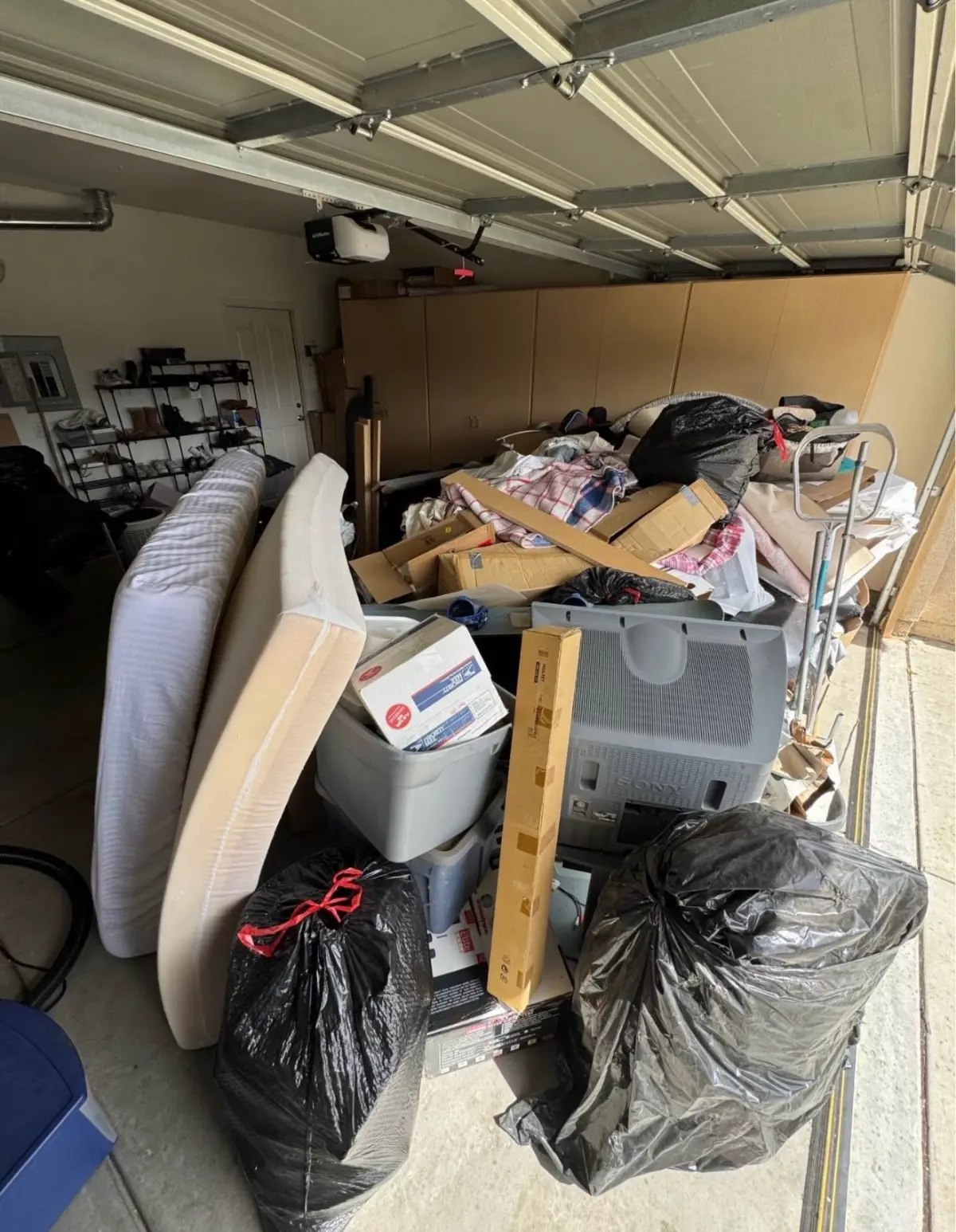 Chandler garage with a mattress and box spring, a CRT TV, boxes and trash bags piled in front of tan storage cabinets
