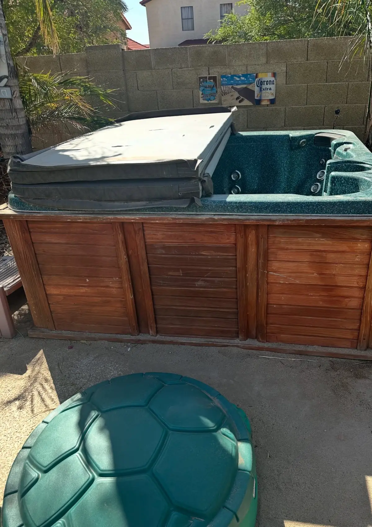 A green speckled hot tub with a redwood skirt and a folded cover against a block wall in a Chandler backyard