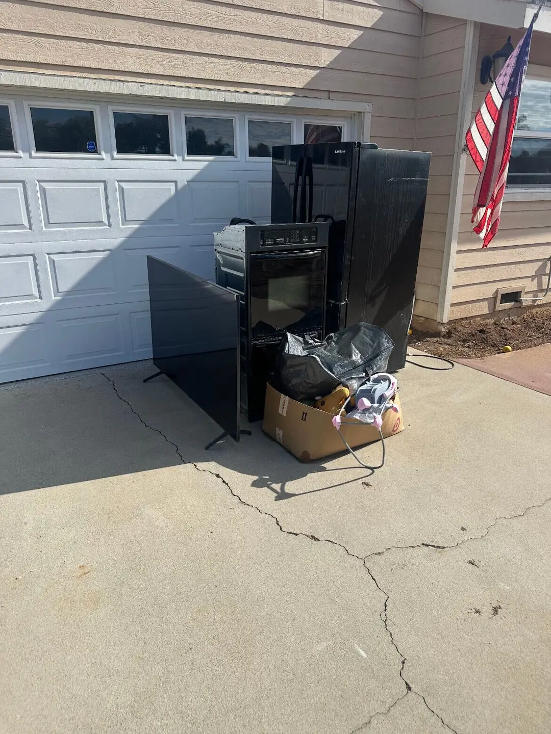 A black refrigerator, a wall oven, a flat-screen TV and a box on a Gilbert driveway in front of a white garage door