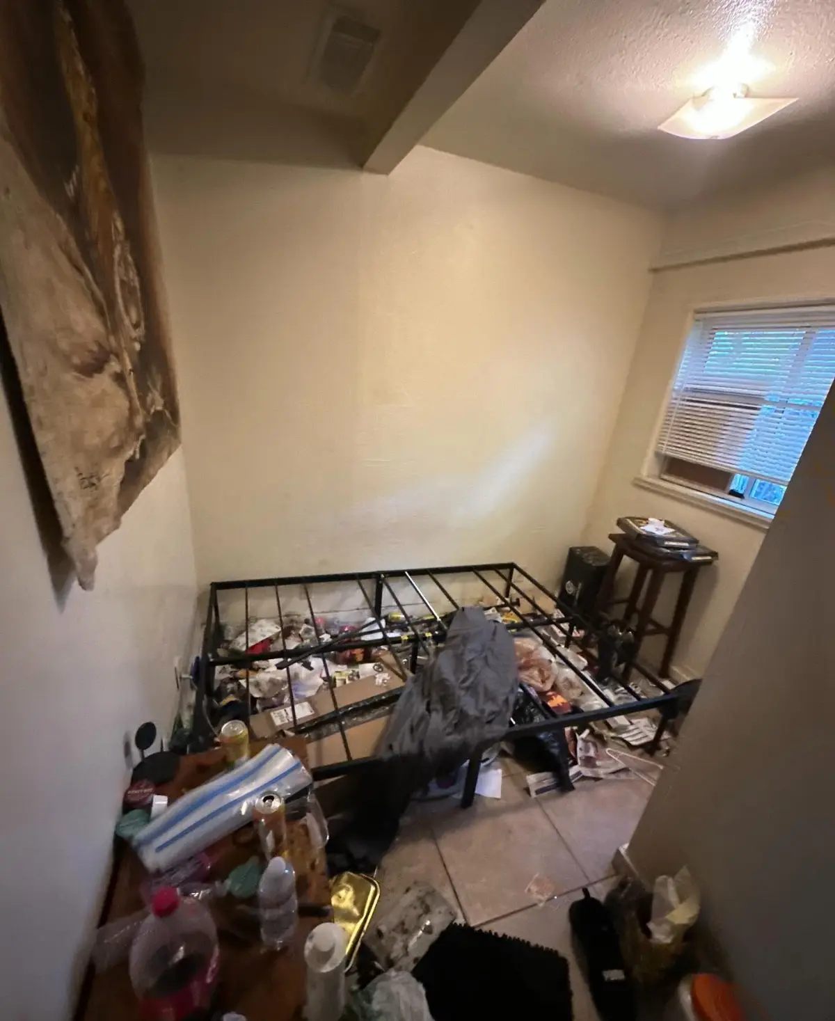A Gilbert bedroom with a bare metal bed frame over bagged contents, bottles and refuse on tan tile