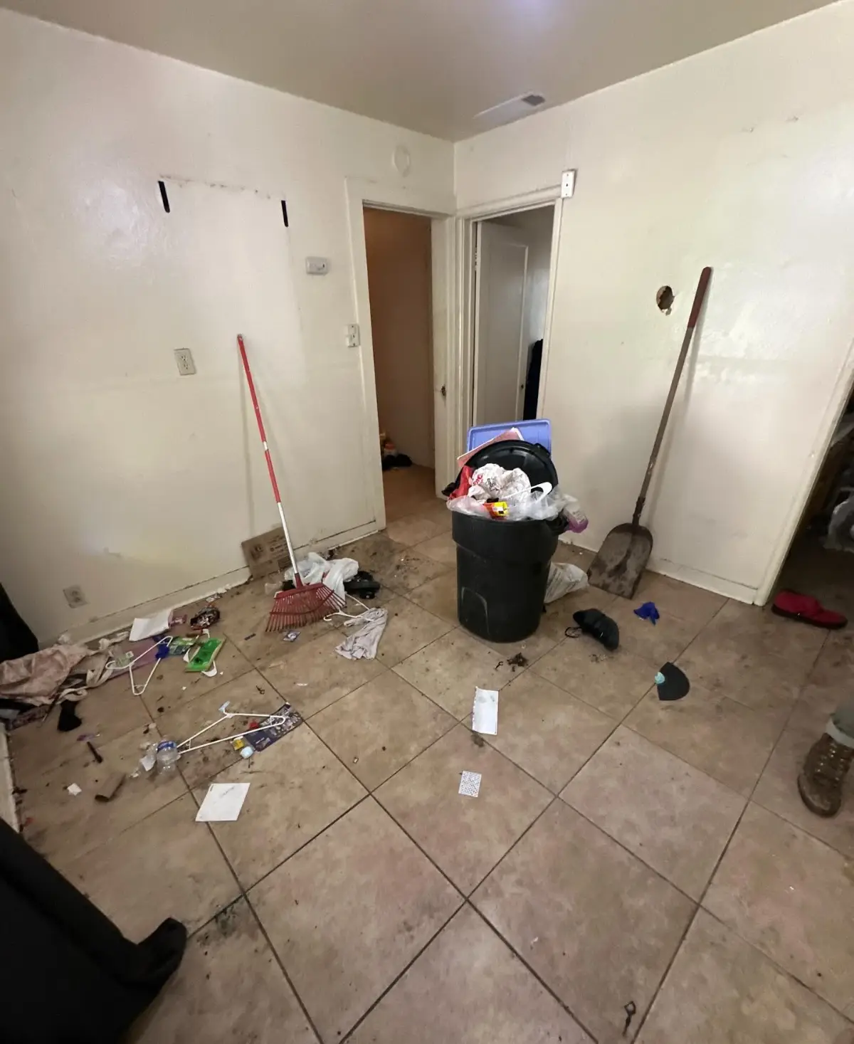 A Gilbert kitchen entry with a trash can, a broom and shovel, hangers and loose refuse on the tile