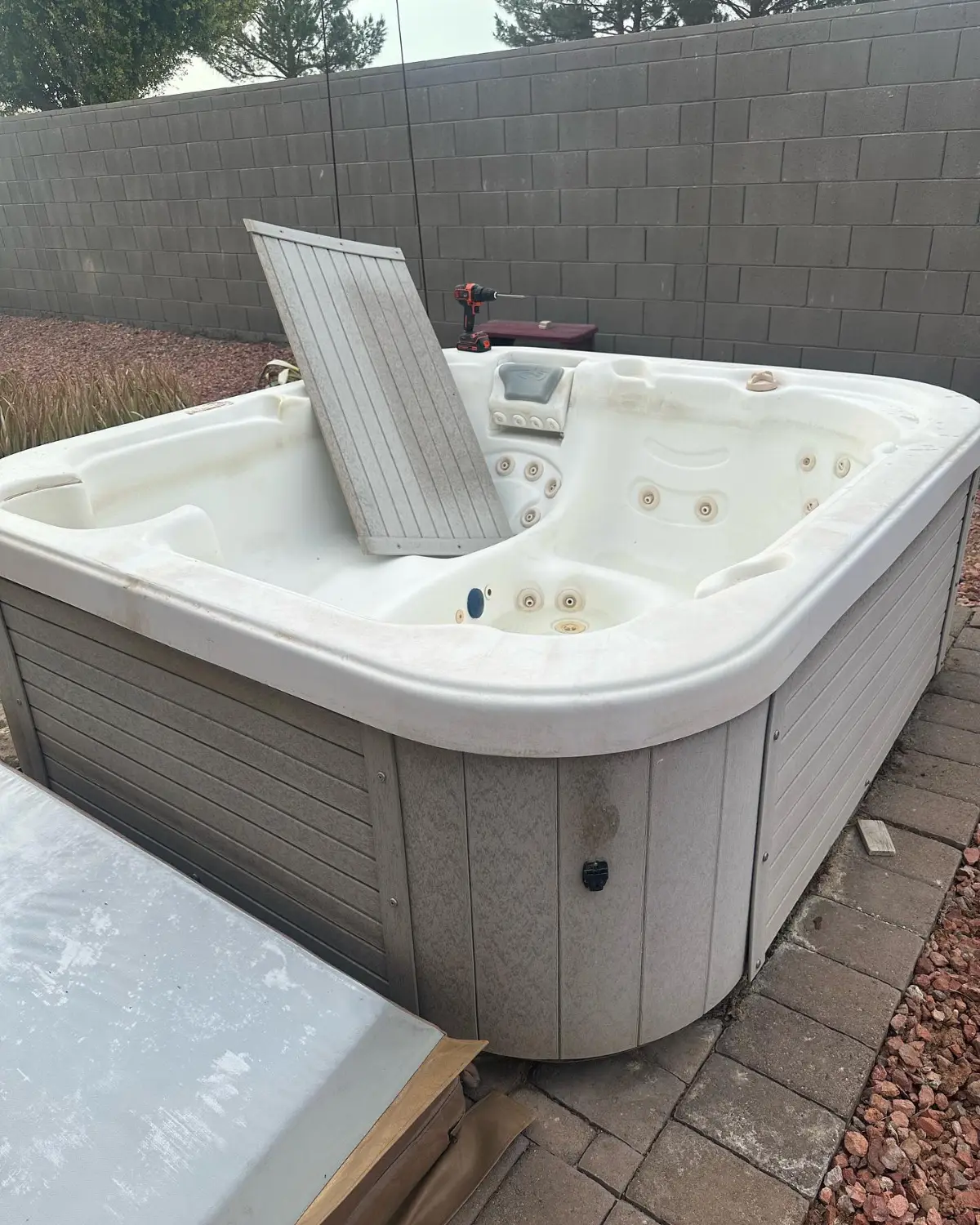 A white hot tub with a gray composite skirt on a paver patio by a block wall in a Gilbert backyard