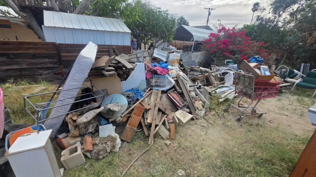 A backyard junk pile of a mattress, lumber, cinder blocks, a shopping cart and a cabinet along a fence at a Goodyear home