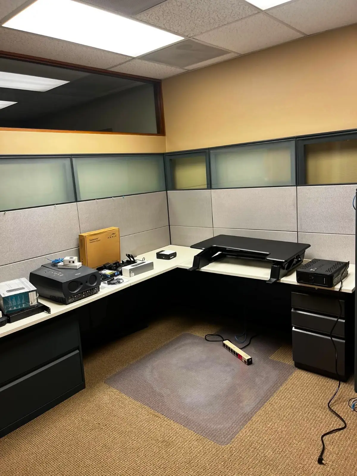 A cubicle workstation in the same Mesa office with panels, a corner desk, a projector and networking equipment