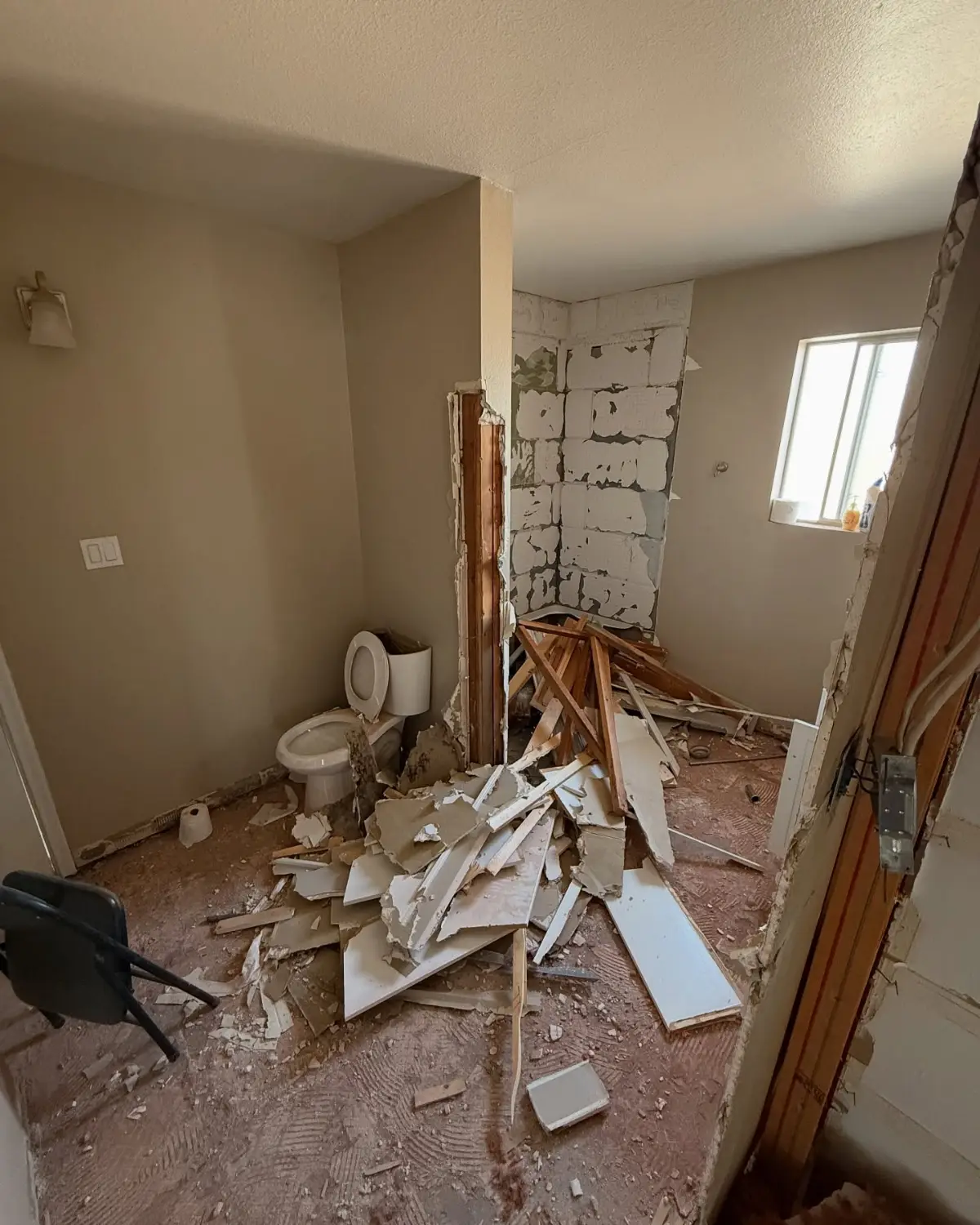 Bathroom in the same Mesa remodel with drywall, lumber and trim piled around the toilet and the shower stripped to the block