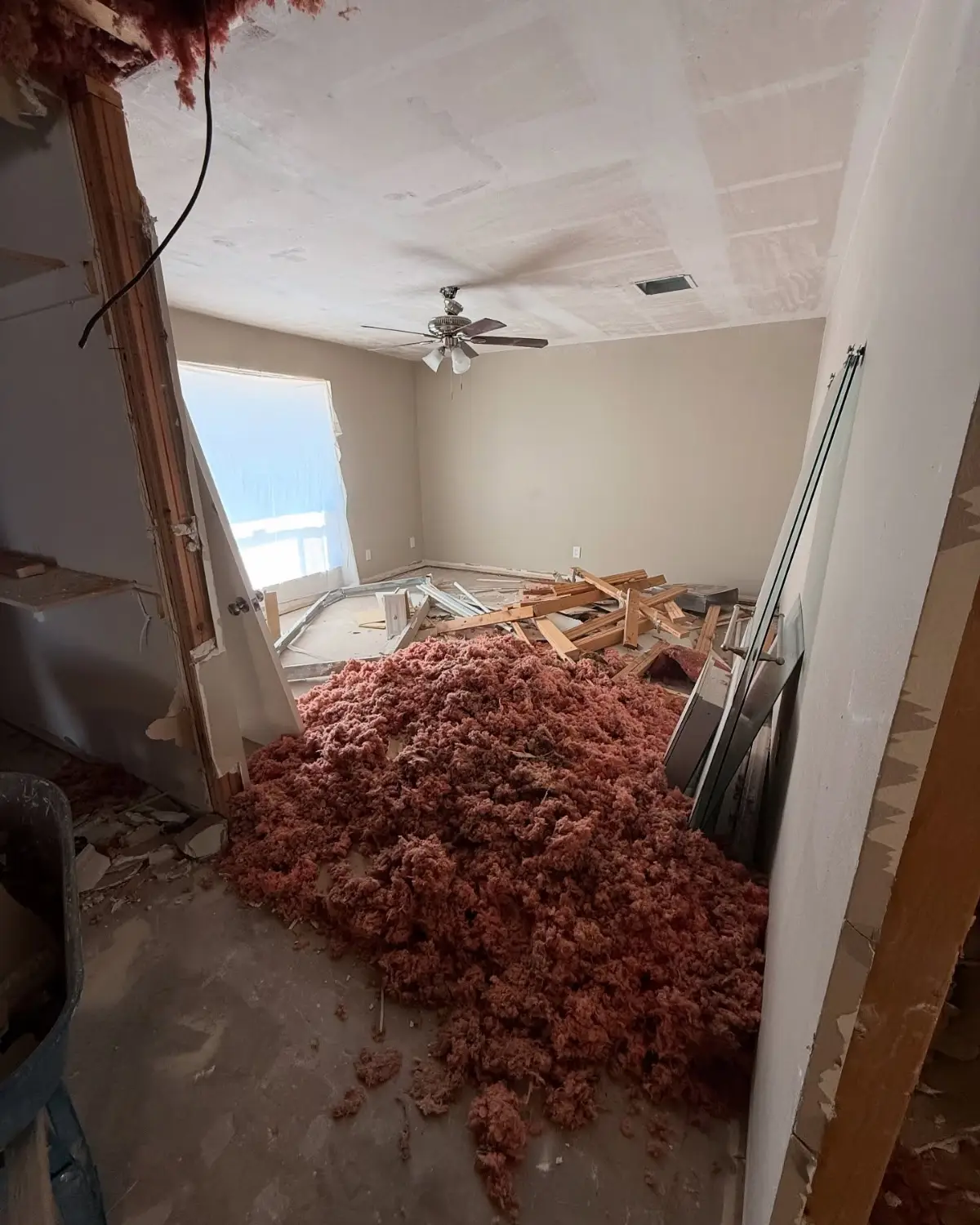 Second bedroom of the same Mesa remodel buried in pink blown insulation with lumber and a door on top