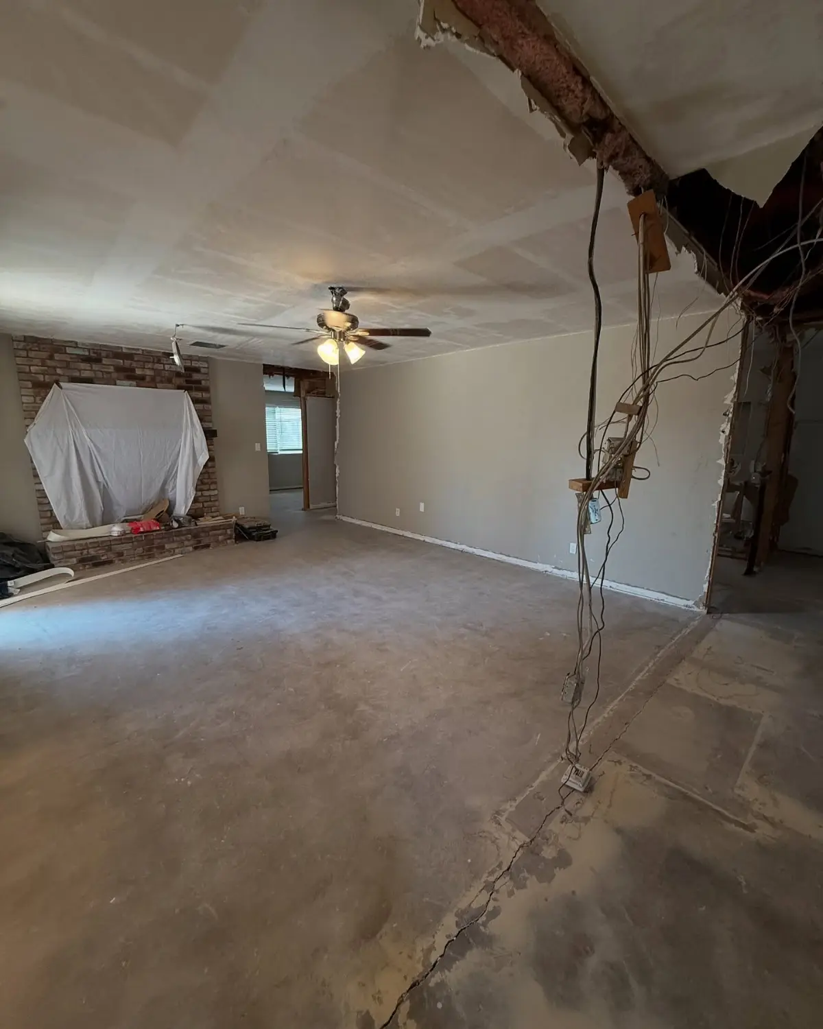 The same Mesa living room with the debris gone and the slab clear; the wiring stays for the electrician