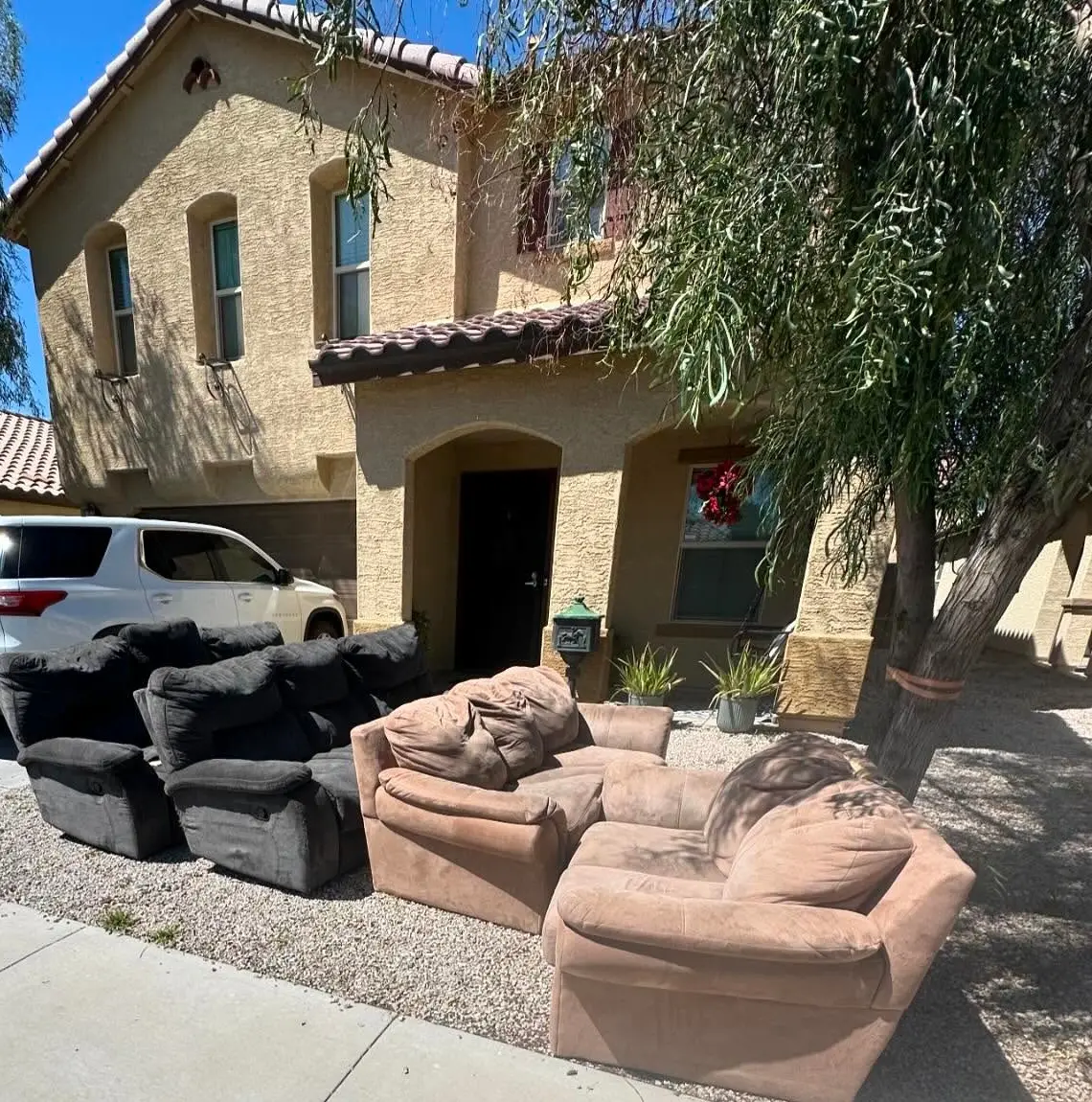Two black recliners, a tan sofa and a loveseat on the front gravel of a Mesa home