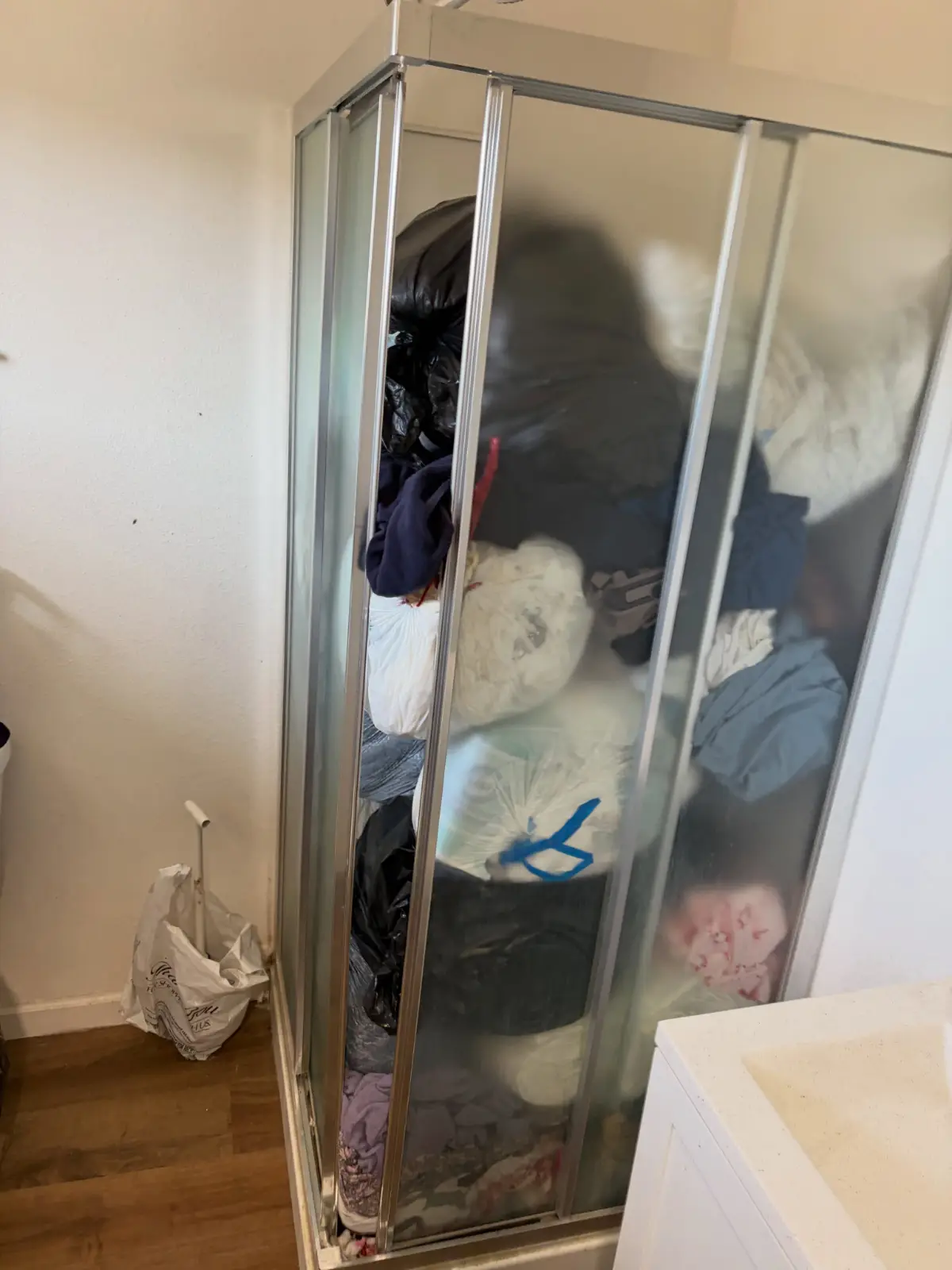 Corner shower stall in the same Mesa apartment packed floor to ceiling with bagged clothing and trash bags