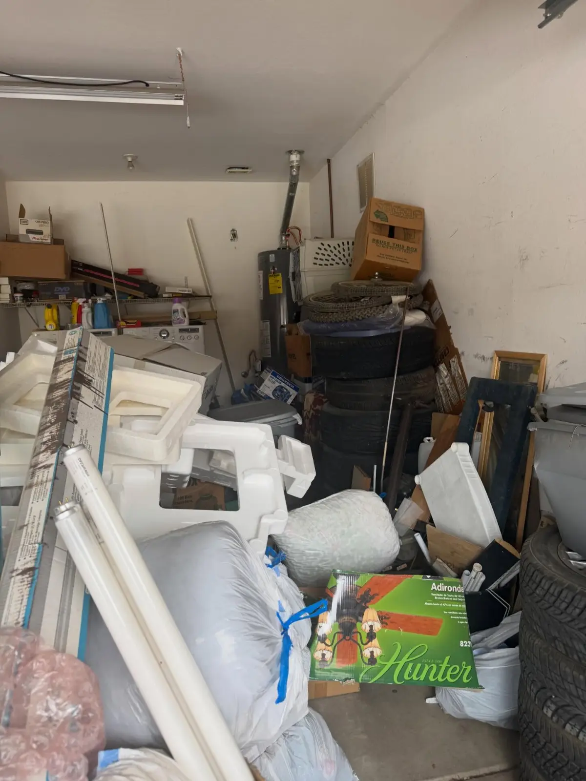 Mesa garage bay filled with foam packing, bagged items, tires, boxes, a mirror frame and tubs in front of the washer and dryer