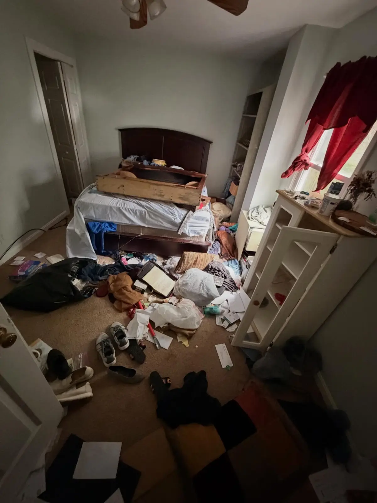 Bedroom in a Mesa home before a hoarding cleanout, with a bed frame and mattress, a shelving unit, clothing, shoes, papers, and bagged belongings covering the floor