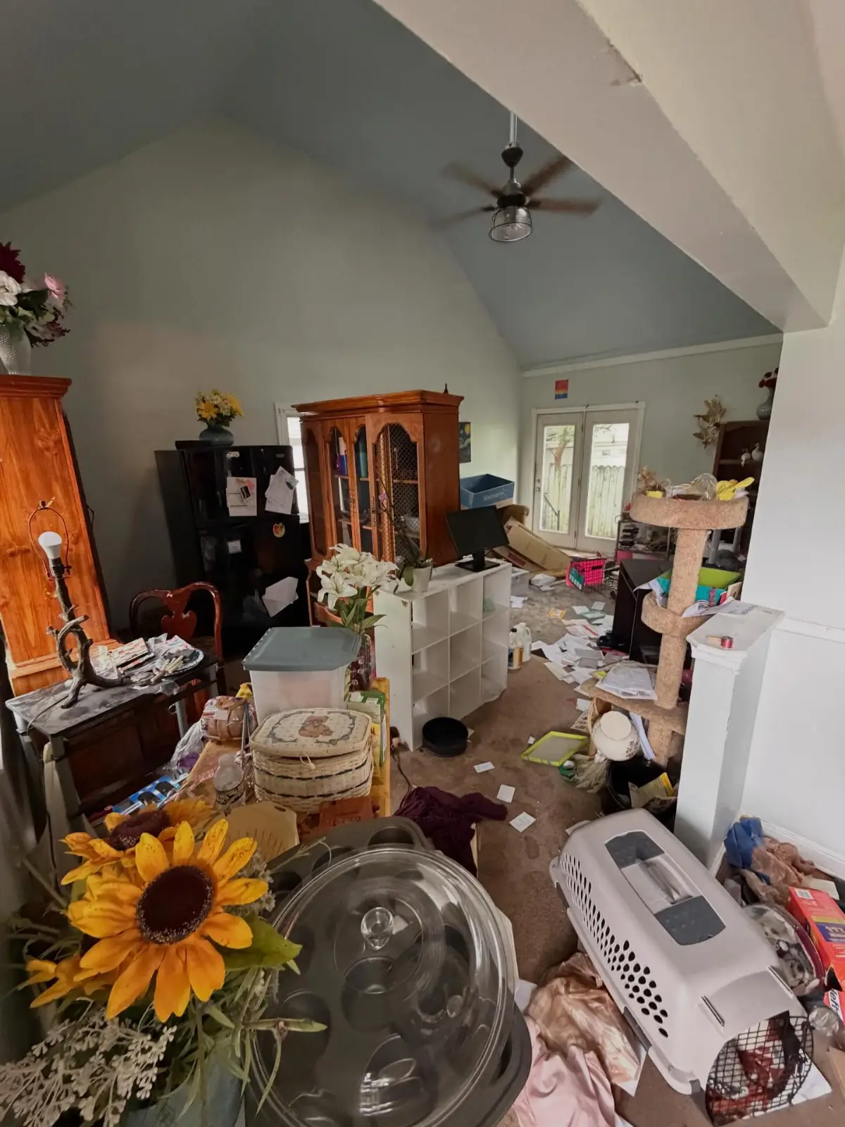 Vaulted living room in a Mesa home before a hoarding cleanout, filled with a china cabinet, a cube shelving unit, a cat tree, storage bins, a pet carrier, and stacked household belongings