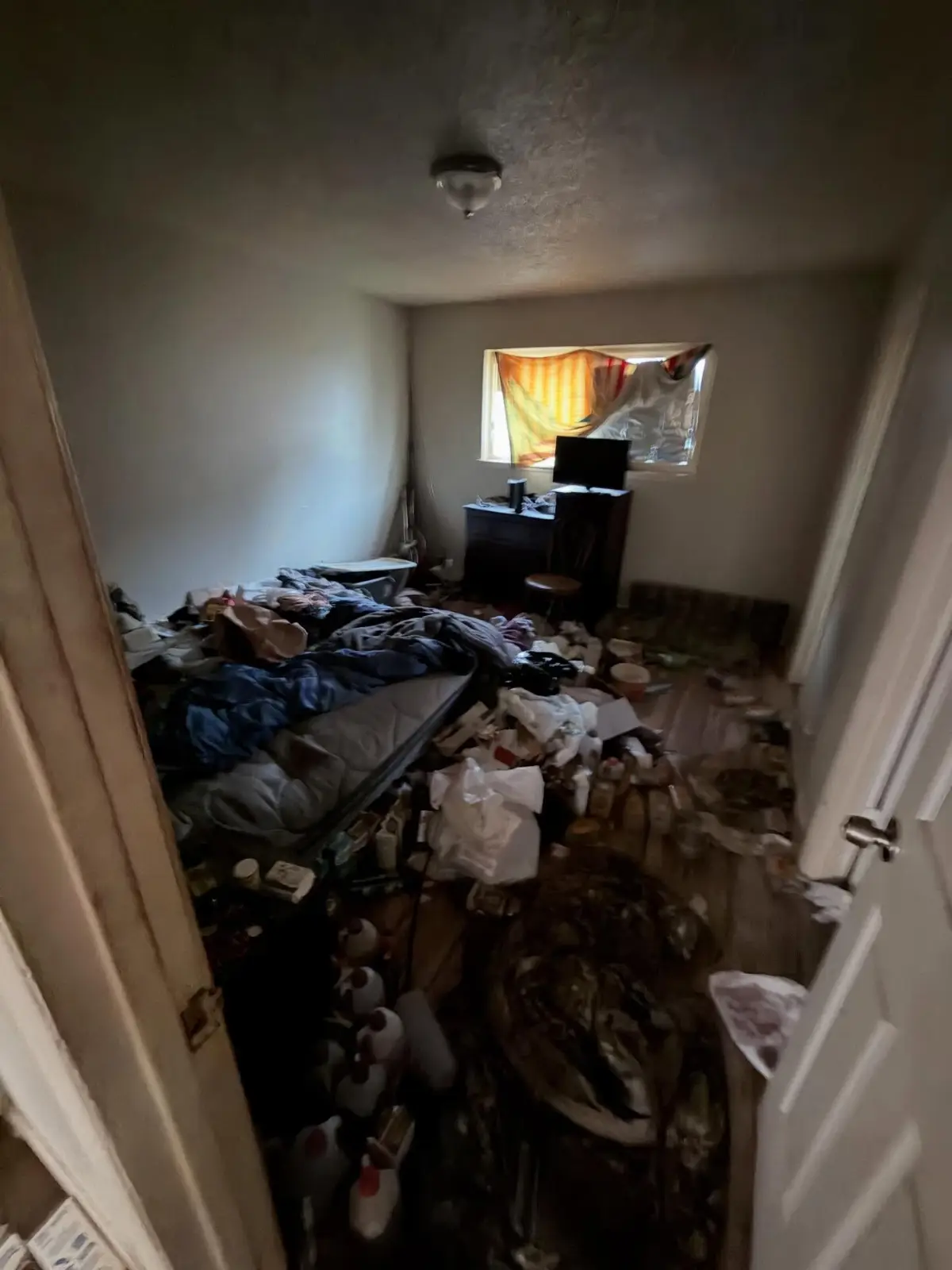 A hoarded Mesa bedroom with a bed buried under clothing, bags and boxes and refuse covering the floor