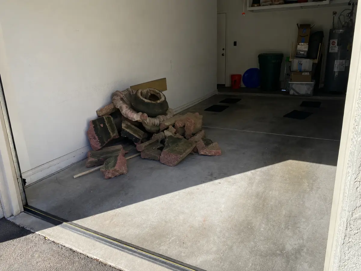 Broken lava-rock landscape edging and a cracked concrete urn heaped on a Mesa garage floor