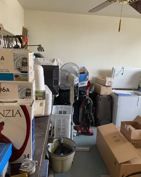 Boxes, household belongings, fans, a vacuum, and storage items in a Mesa room before junk removal