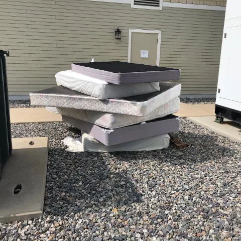 Stack of mattresses and box springs beside a Mesa building before pickup
