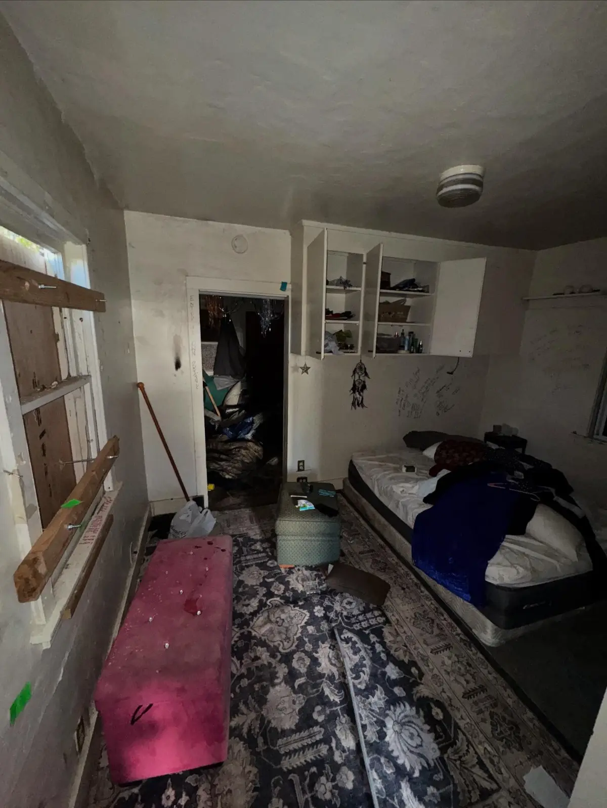 A bedroom in the same Mesa rental unit with a mattress and box spring, a pink bench, an ottoman and clothing on the floor