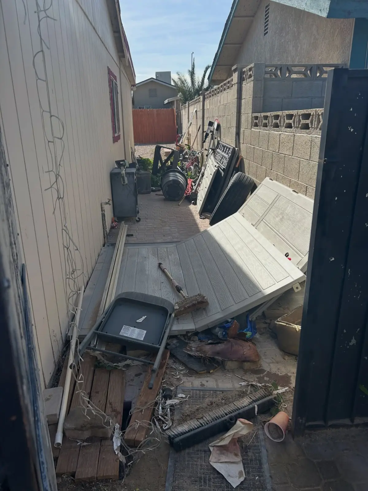 Narrow gated side yard at a Paradise Valley home blocked with patio panels, planters, piping and scattered debris