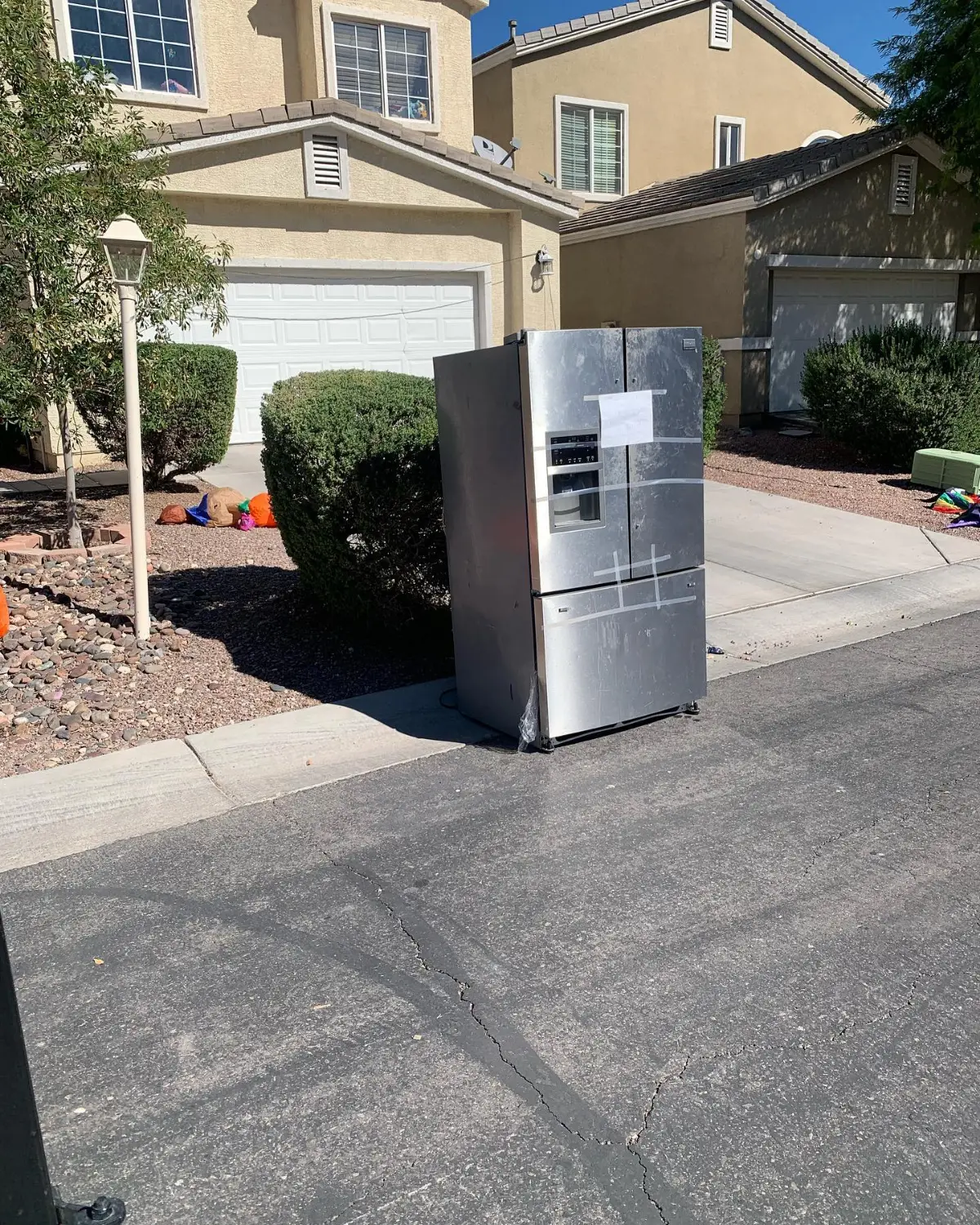 A stainless French-door refrigerator standing at the curb on the street in front of a two-story Peoria house with a white garage door