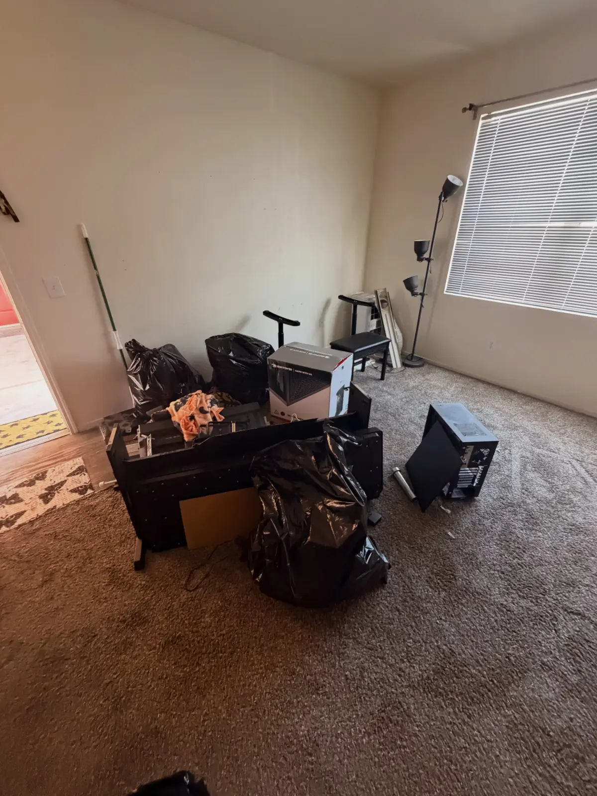A desk, computer tower, floor lamp and bagged items on the carpet of a Peoria bedroom