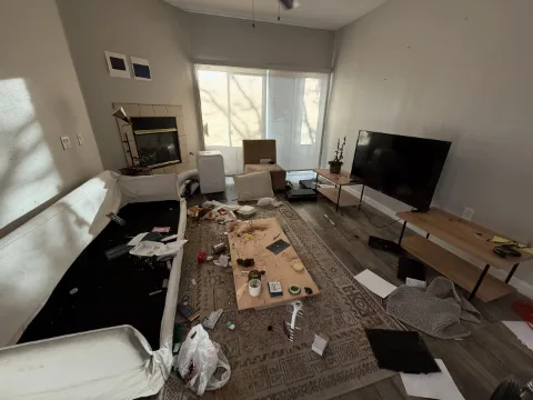 A Phoenix apartment living room with a torn sofa, a TV, tables and refuse across a rug by the corner fireplace