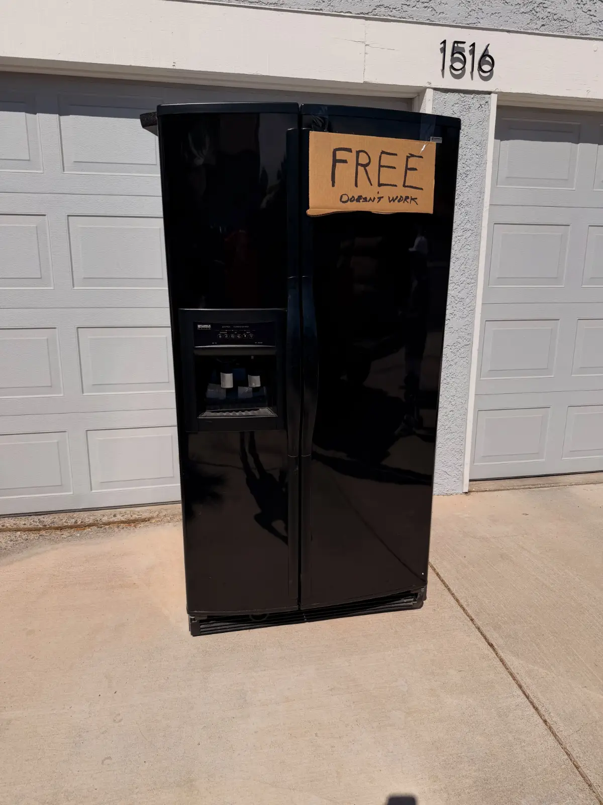 A black side-by-side refrigerator marked FREE standing on a Phoenix driveway in front of the garage
