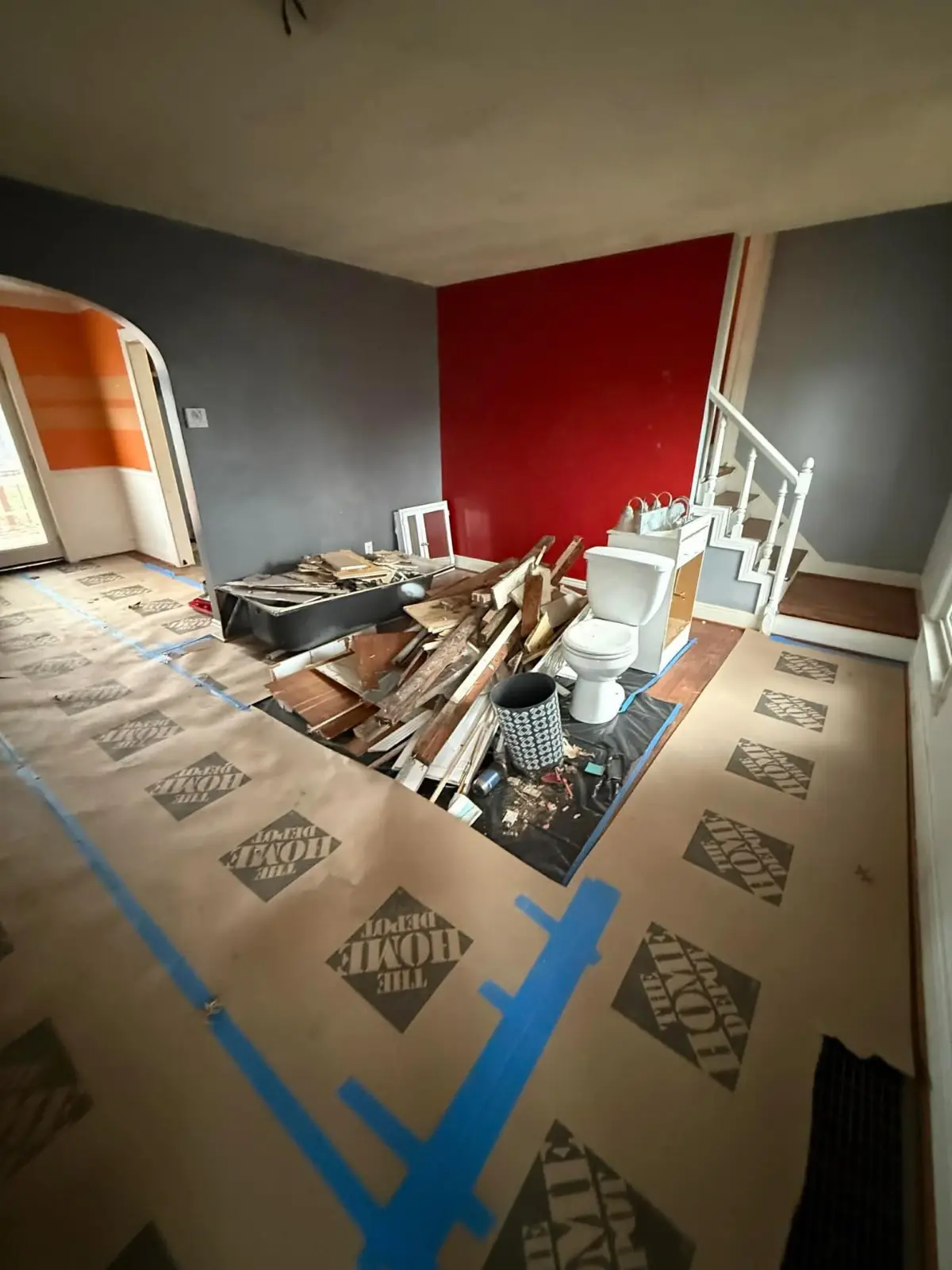 Bathroom tear-out debris — tub, toilet, vanity and lumber — piled on a protected living room floor in a Phoenix home