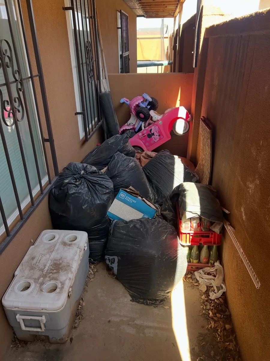 Household junk, bags, children's ride-on toys, and a cooler in a Phoenix side yard before removal