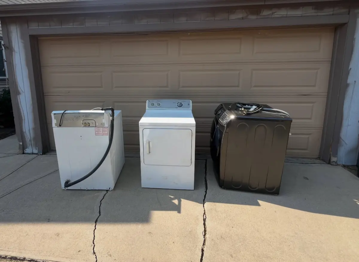A top-load washer, a dryer and a black front-load washer in front of a tan garage door in Scottsdale