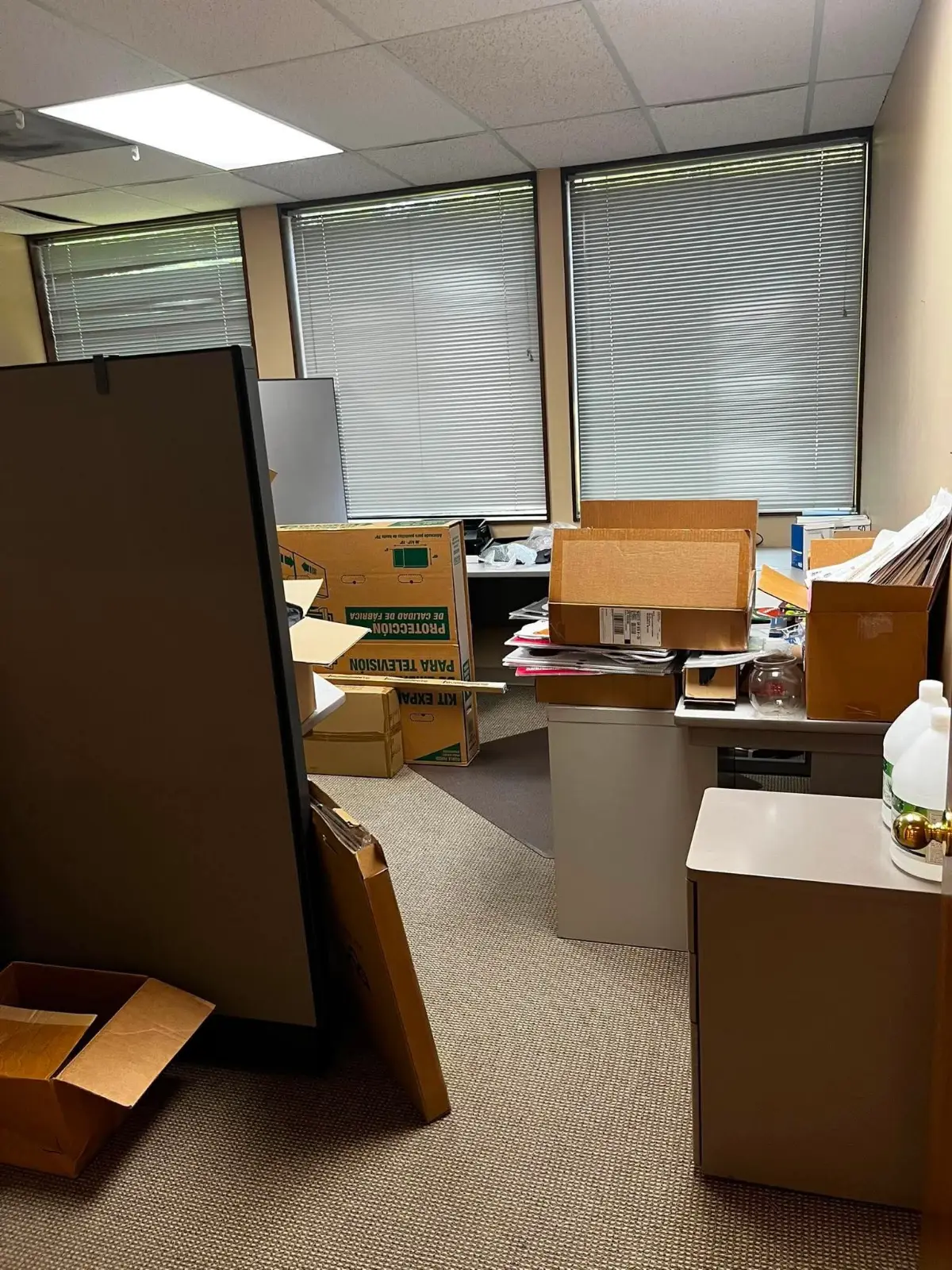 A Scottsdale office with a cubicle panel against the wall, moving boxes, filing cabinets and paperwork across the desks and floor