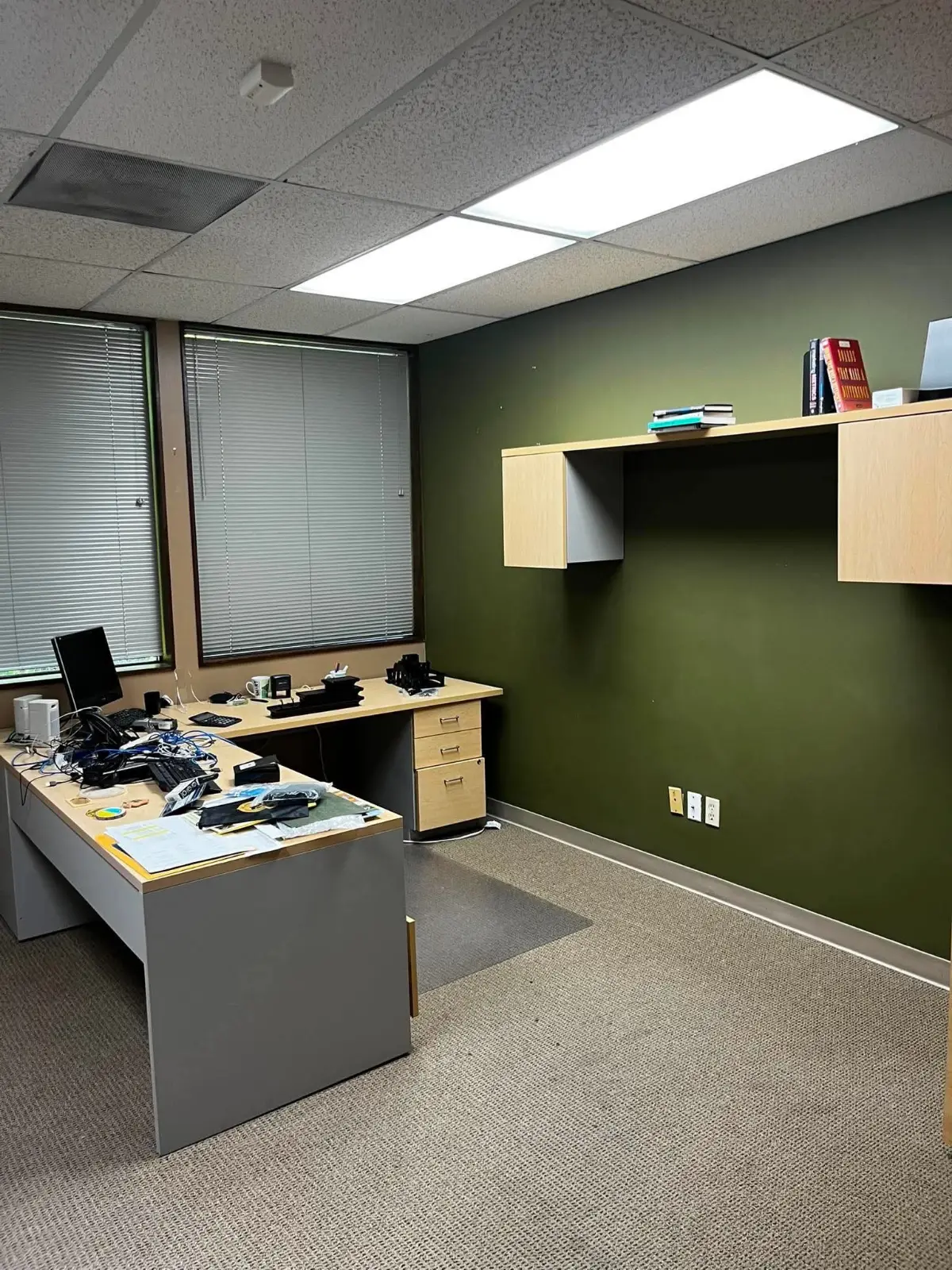 A private office in the same Scottsdale suite with an L-shaped desk covered in cables and boxes and a wall-mounted hutch above it