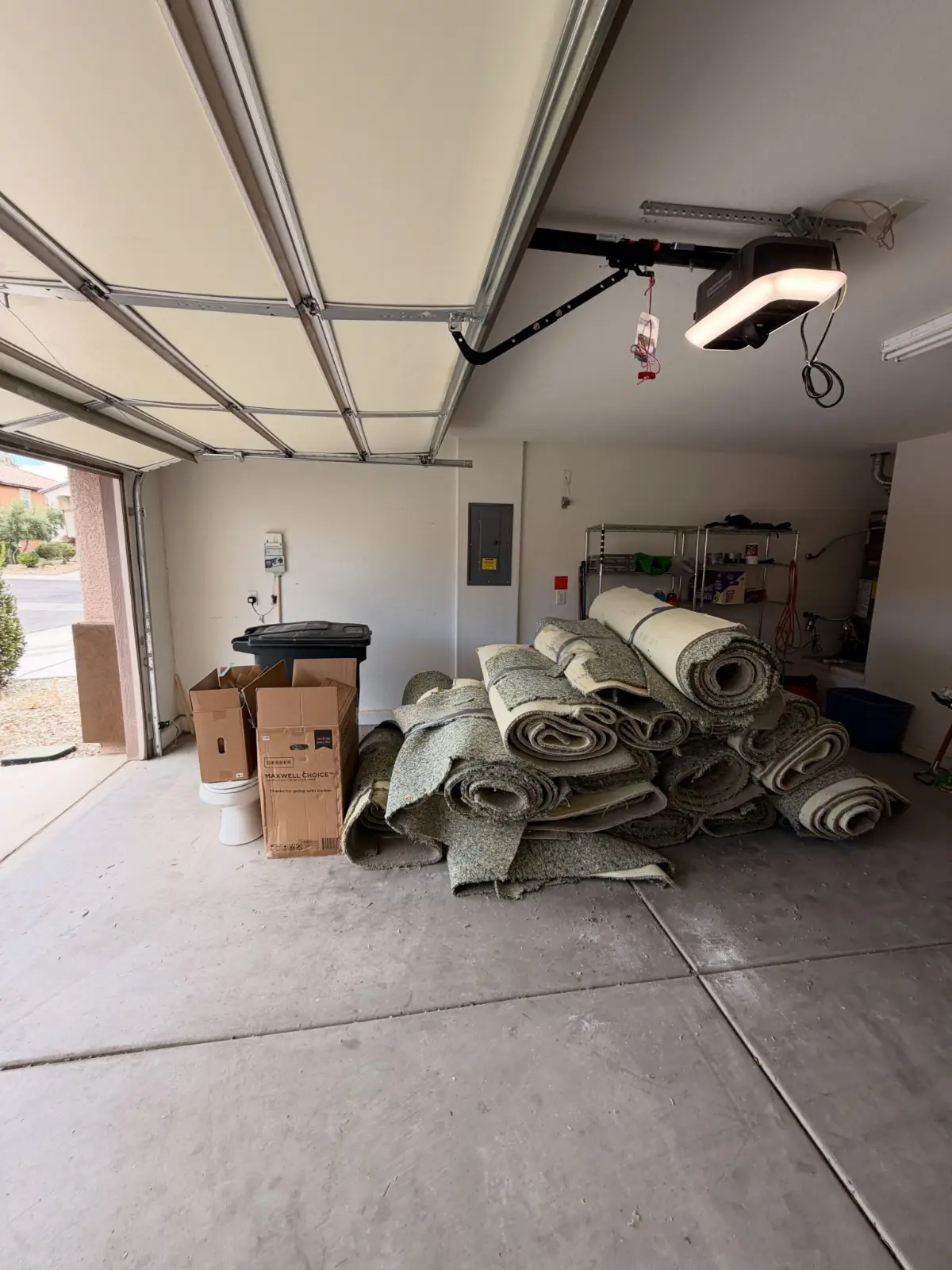 Rolled carpet from a flooring tear-out piled in a Scottsdale garage with boxes and a toilet alongside