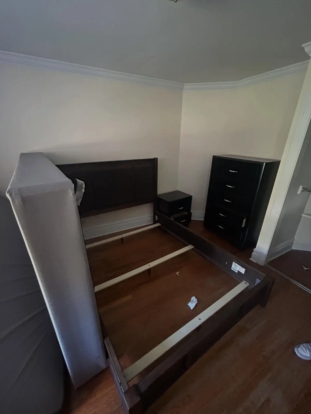 A disassembled bed frame, nightstand and tall black chest of drawers on the hardwood floor of a Scottsdale bedroom before removal