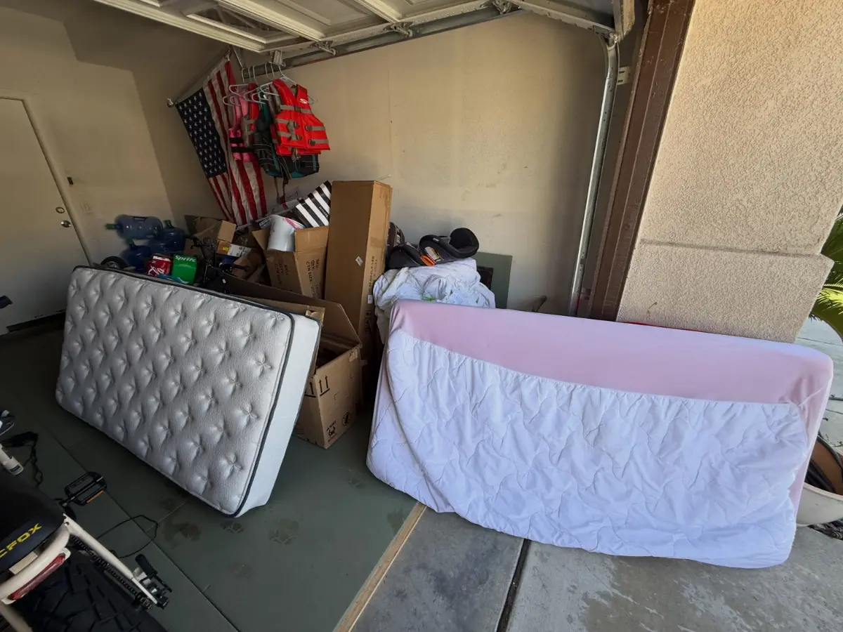 Scottsdale garage bay with two mattresses, moving boxes, a car seat and bedding on rubber floor mats