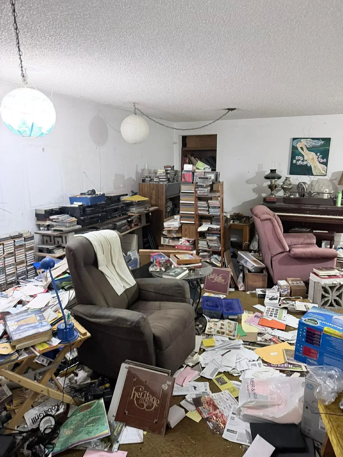 A hoarded Scottsdale living room with a piano, recliners, racks of cassettes and CDs and papers covering the floor