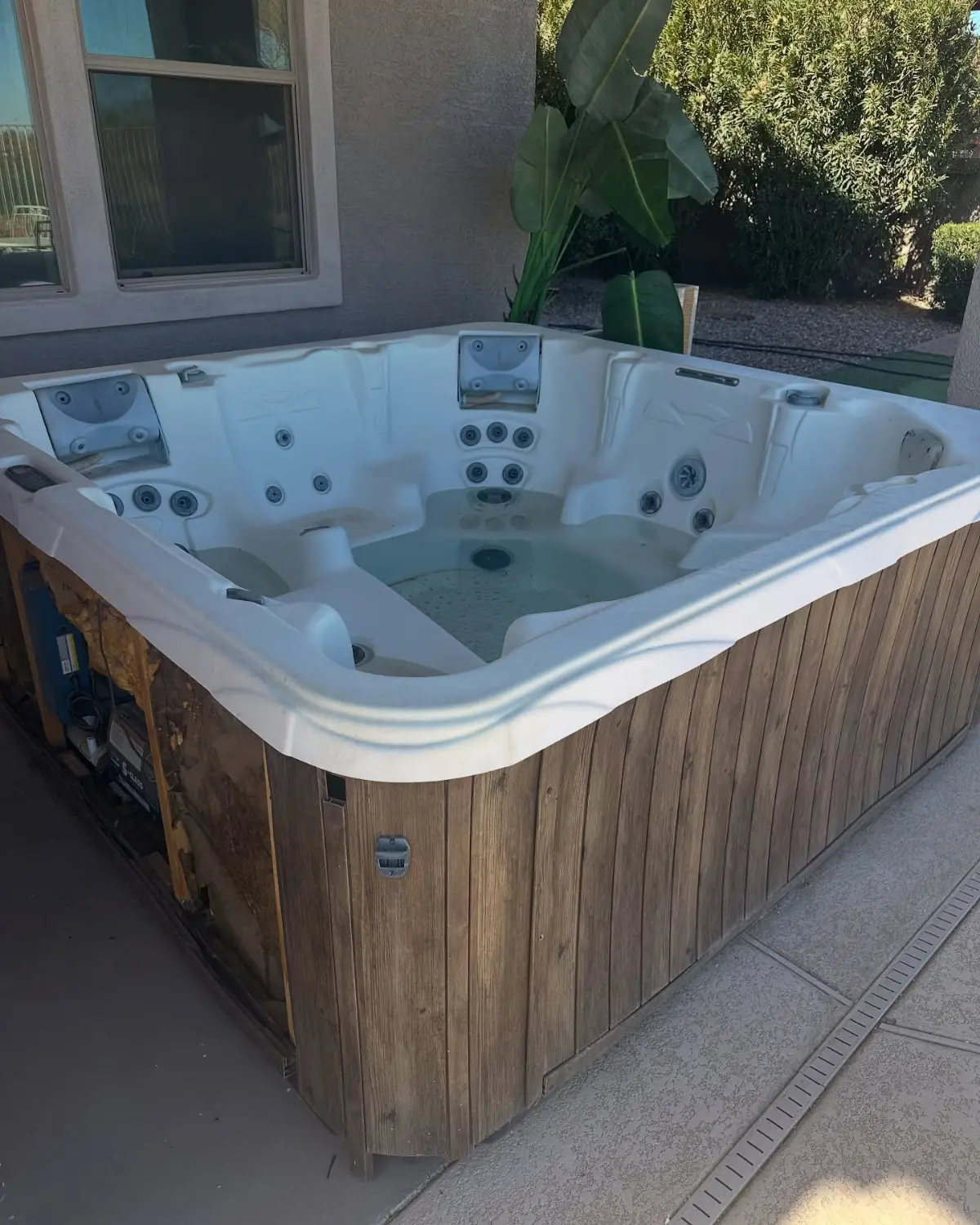 A white acrylic hot tub with a weathered wood skirt on a back patio in Scottsdale beside a window