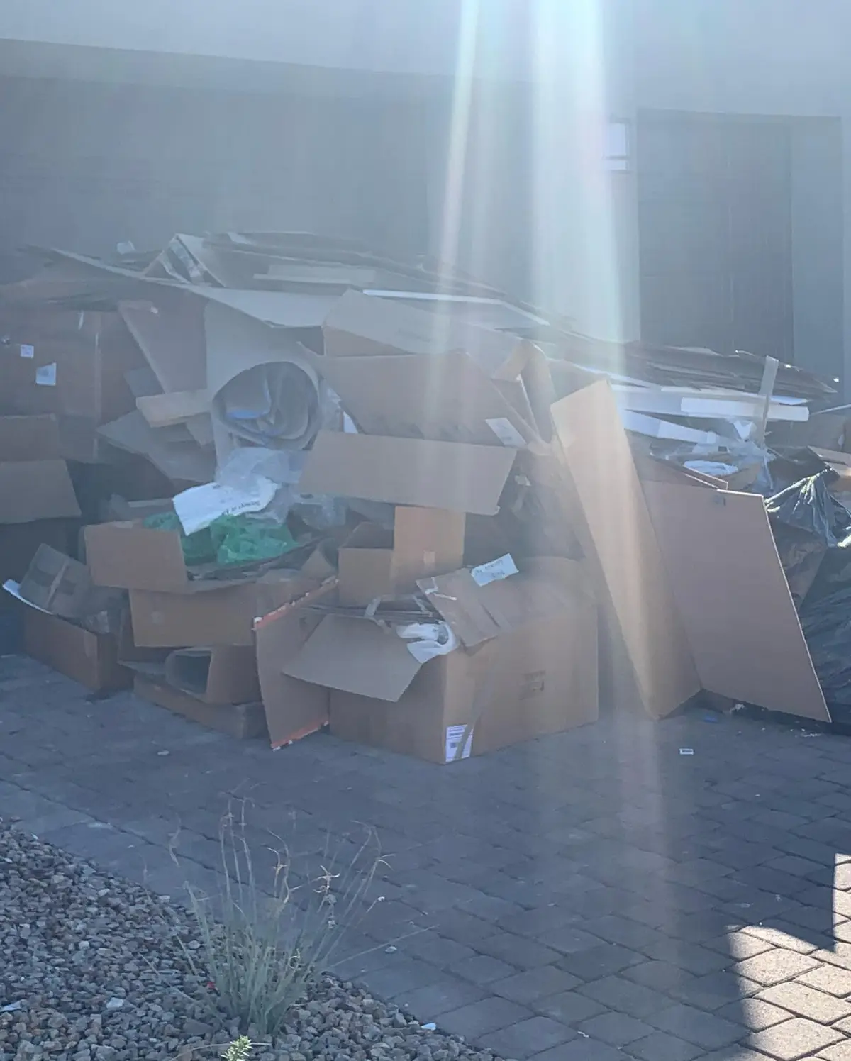 A tall pile of flattened cardboard boxes, packing foam and black trash bags against a dark garage door on a Scottsdale paver driveway