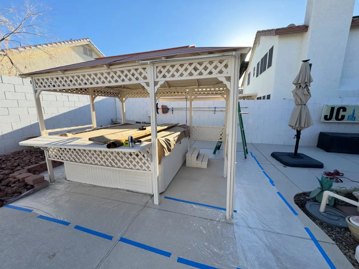 A white lattice gazebo standing over a hot tub on a Scottsdale back patio with floor protection laid out