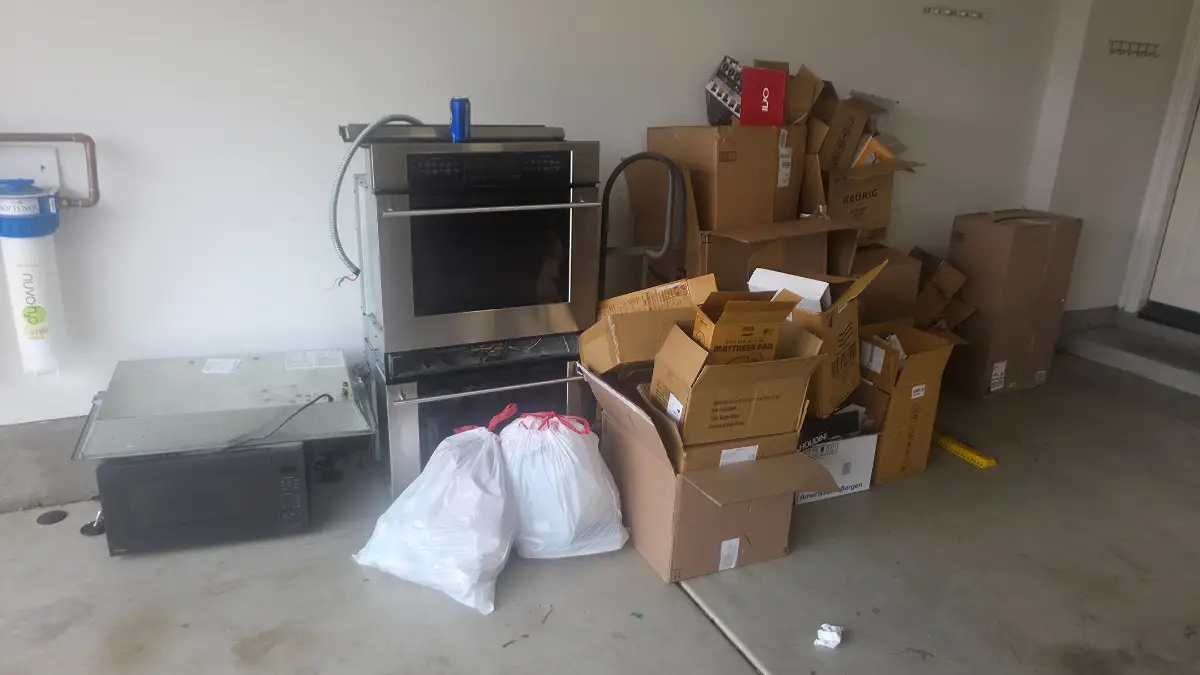 A Tempe garage with a double wall oven, a microwave, stacked boxes and bagged items against the wall