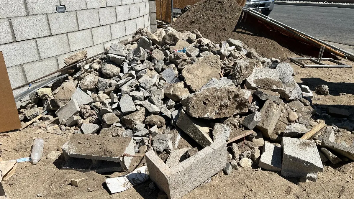A pile of broken concrete and cinder block rubble against a block wall on a dirt lot in Tempe