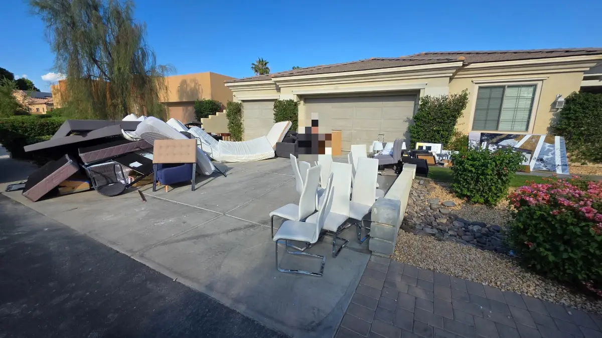 A Tempe driveway staged with mattresses, sofas, white dining chairs, a headboard and framed artwork in front of a two-car garage