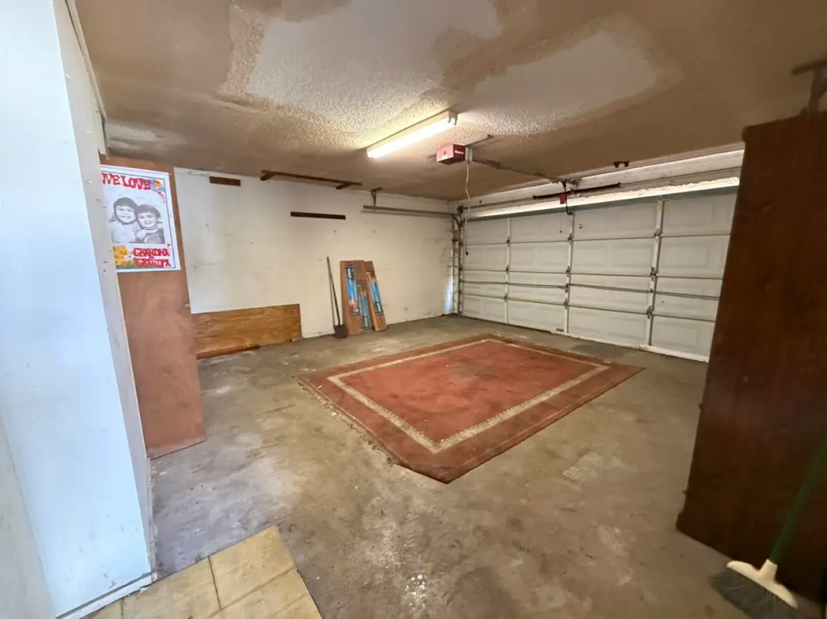 The same Tempe garage cleared to the slab with an area rug laid out; a plywood panel and a broom remain